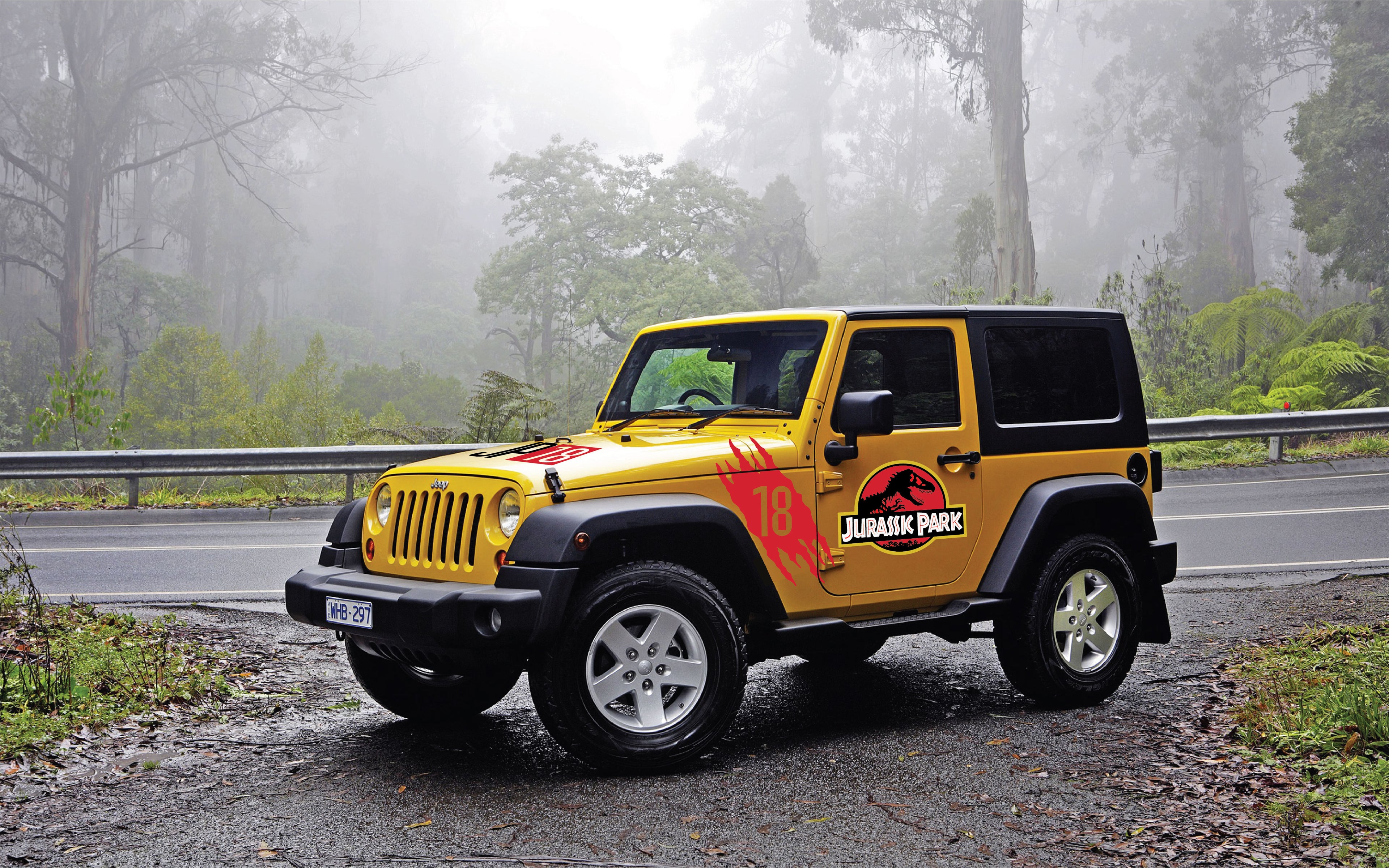 Yellow Jeep Wrangler parked on the side of the road in a jungle with a set of Jurassic Park Original colors logos on the doors and numbered scratch stickers on the front side and a JP18 hood decal.